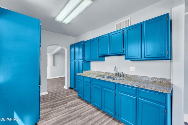 4301 Hueco Ave, El Paso, TX 79903 - kitchen with a sink, blue cabinetry, arched walkways, light wood finished floors, and baseboards