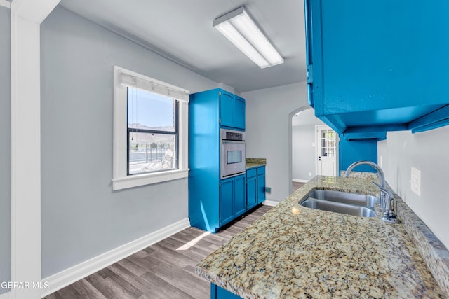 4301 Hueco Ave, El Paso, TX 79903 - kitchen featuring oven, blue cabinets, a sink, arched walkways, and wood finished floors