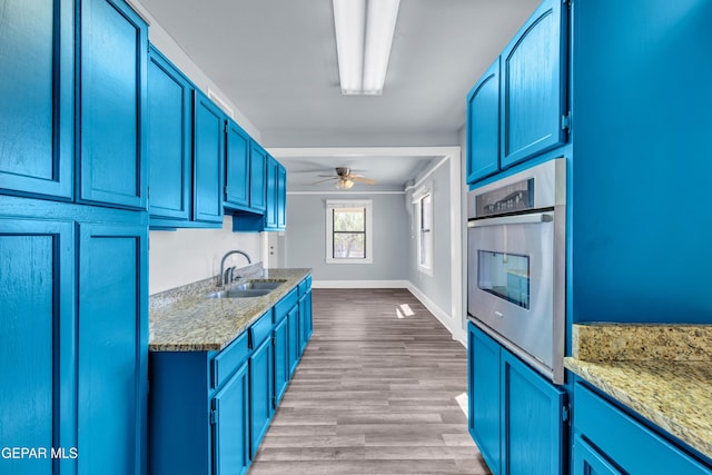 4301 Hueco Ave, El Paso, TX 79903 - kitchen with oven, a sink, blue cabinetry, ceiling fan, and light wood finished floors