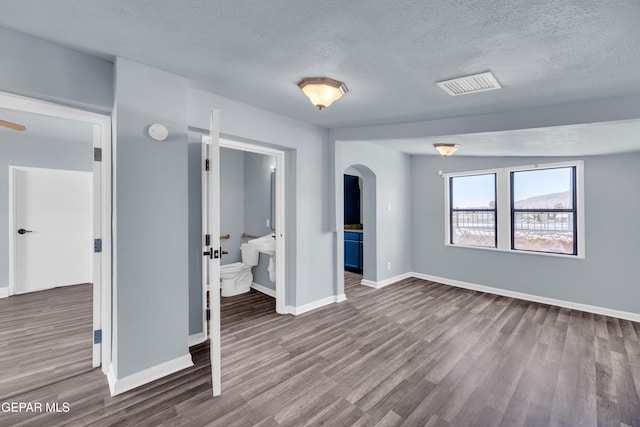 4301 Hueco Ave, El Paso, TX 79903 - unfurnished bedroom with a textured ceiling, arched walkways, wood finished floors, baseboards, and connected bathroom