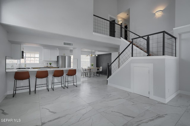 7413 Le Conte Dr, El Paso, TX 79912 - kitchen featuring freestanding refrigerator, light marble finish floors, a high ceiling, a breakfast bar, and white cabinets