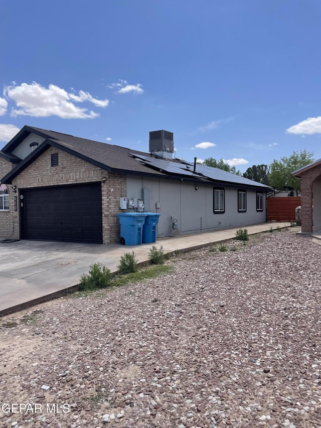 472 Valle Suave Dr, Socorro, TX 79927 - view of side of home featuring roof mounted solar panels, an attached garage, concrete driveway, central AC unit, and brick siding