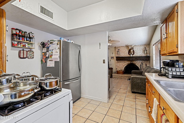 1664 Lou Graham Dr, El Paso, TX 79936 - kitchen featuring white gas range oven, light tile patterned flooring, brown cabinetry, a fireplace, and light countertops