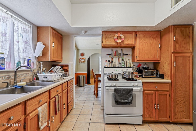 1664 Lou Graham Dr, El Paso, TX 79936 - kitchen with white gas range, a sink, arched walkways, light tile patterned flooring, and light countertops