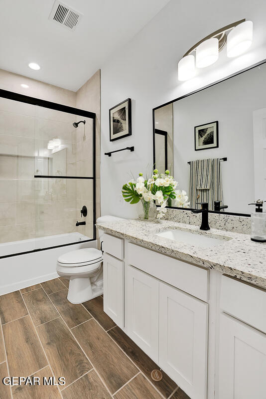 12849 Middlesbrough Ave, Horizon City, TX 79928 - bathroom featuring toilet, wood finish floors, combined bath / shower with glass door, vanity, and recessed lighting