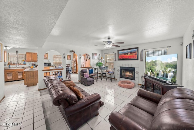 11968 Frances Scobee Dr, El Paso, TX 79936 - living area featuring a ceiling fan, a textured ceiling, arched walkways, light tile patterned floors, and a tiled fireplace