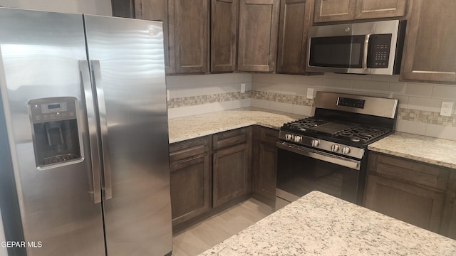 12869 Woolstone Dr, El Paso, TX 79928 - kitchen with appliances with stainless steel finishes, decorative backsplash, dark brown cabinets, and light stone countertops