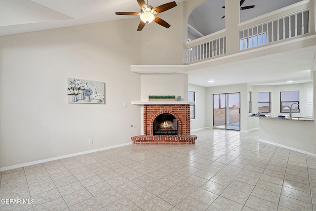 unfurnished living room with ceiling fan, high vaulted ceiling, light tile patterned flooring, a fireplace, and baseboards