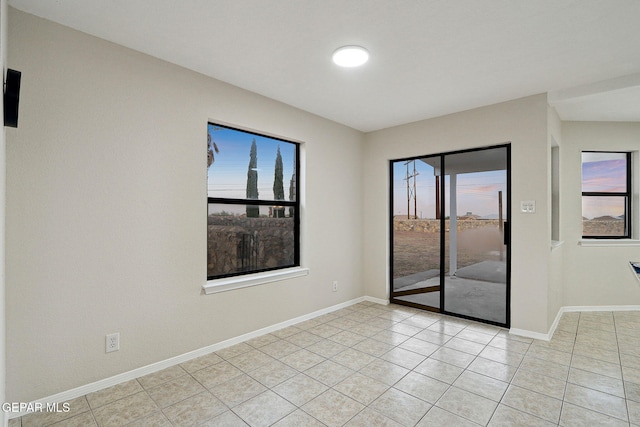 empty room with light tile patterned flooring, plenty of natural light, and baseboards