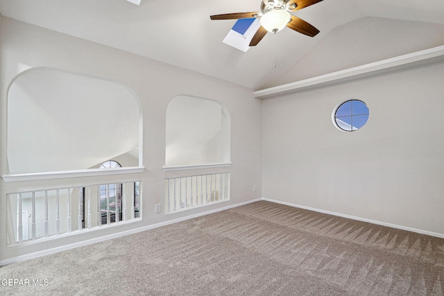 carpeted empty room with ceiling fan, vaulted ceiling, a skylight, and baseboards