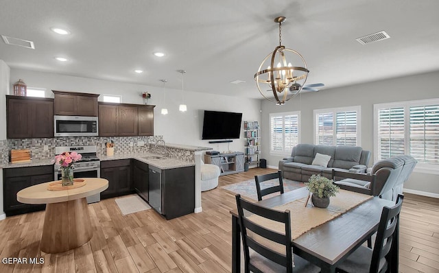 kitchen with stainless steel appliances, a sink, a peninsula, a chandelier, and dark brown cabinets