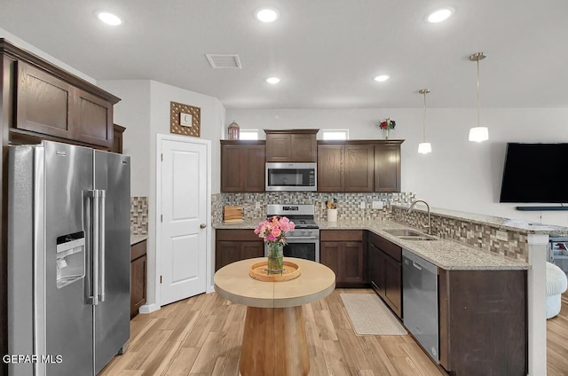kitchen featuring appliances with stainless steel finishes, a sink, a peninsula, decorative backsplash, and dark brown cabinetry