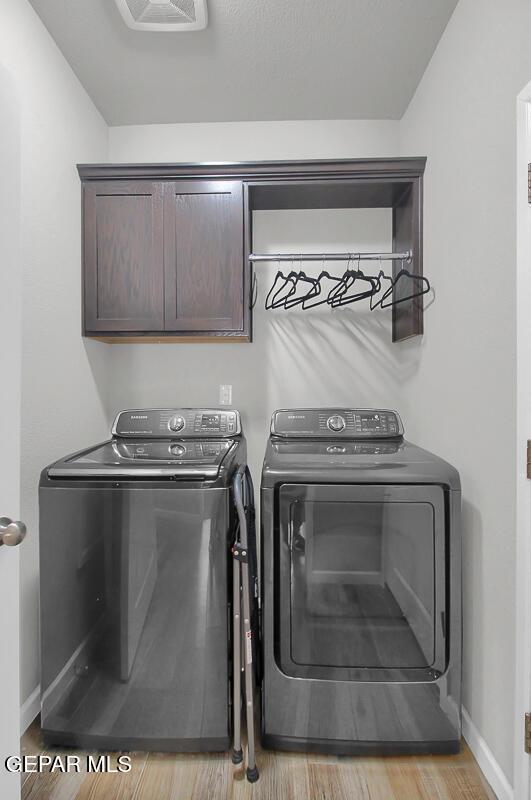 clothes washing area with cabinet space, washing machine and clothes dryer, light wood-type flooring, and baseboards