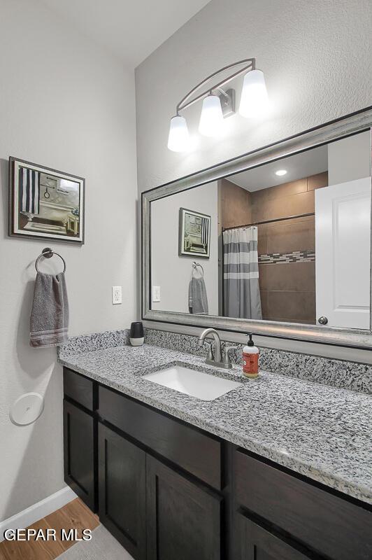 full bath featuring wood finished floors, vanity, tiled shower, and baseboards