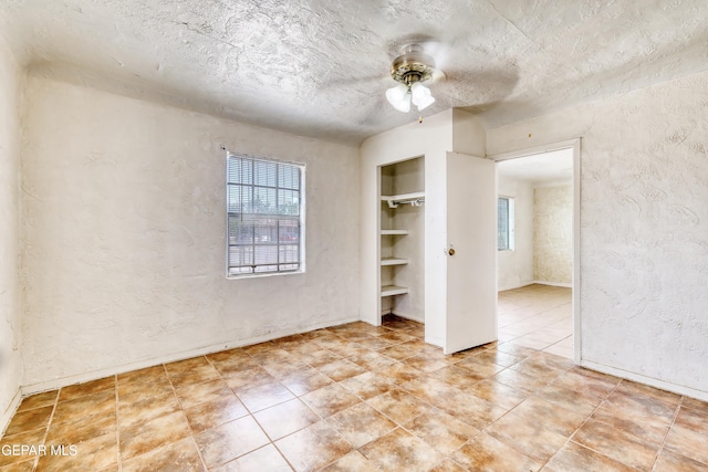 159 Silvas Way, El Paso, TX 79907 - tiled spare room featuring a ceiling fan, built in shelves, a textured wall, and a textured ceiling