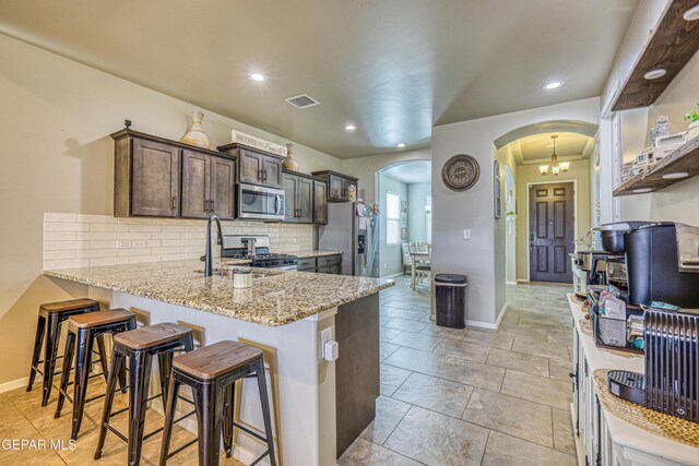 13729 Blackburn Ave, El Paso, TX 79928 - kitchen featuring stainless steel appliances, arched walkways, baseboards, dark brown cabinetry, and tasteful backsplash