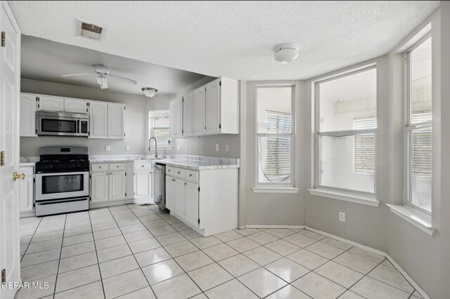 kitchen with stainless steel appliances, light countertops, white cabinetry, light tile patterned floors, and a textured ceiling