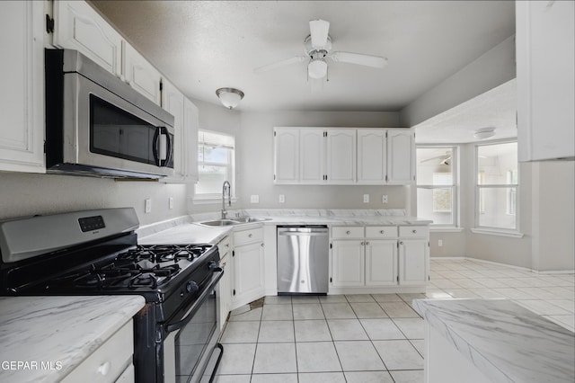 kitchen with stainless steel appliances, a sink, light tile patterned flooring, and white cabinets