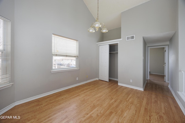 unfurnished bedroom featuring high vaulted ceiling, a chandelier, a closet, light wood-style floors, and baseboards