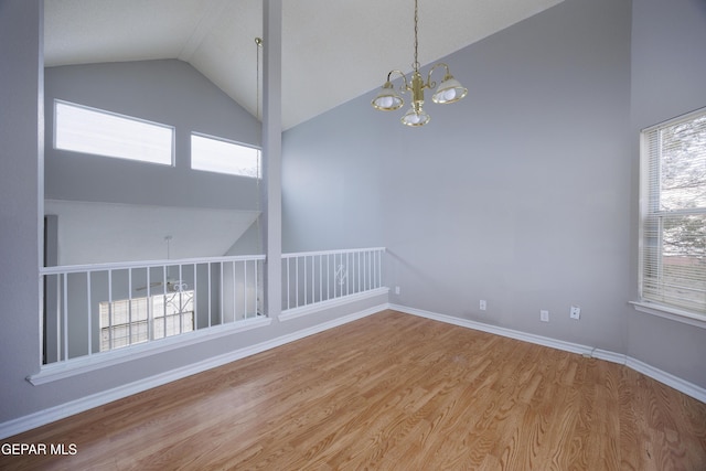 spare room with high vaulted ceiling, a chandelier, wood finished floors, and baseboards