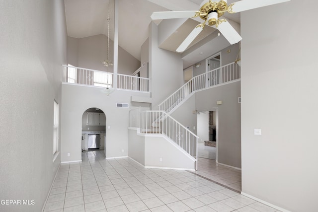 unfurnished living room with a ceiling fan, high vaulted ceiling, tile patterned flooring, arched walkways, and stairs