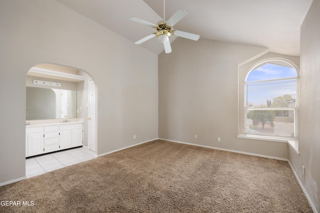 unfurnished bedroom featuring light carpet, arched walkways, lofted ceiling, connected bathroom, and light tile patterned floors