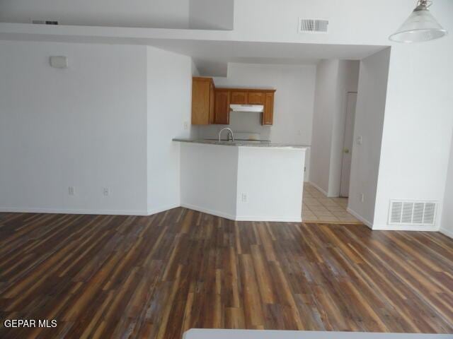 kitchen with wood finished floors, light countertops, under cabinet range hood, brown cabinetry, and baseboards