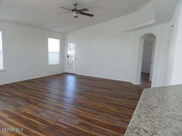 empty room featuring arched walkways, dark wood-type flooring, a ceiling fan, vaulted ceiling, and baseboards