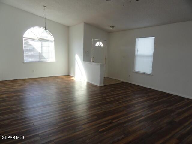 spare room featuring dark wood-type flooring, a ceiling fan, vaulted ceiling, and baseboards