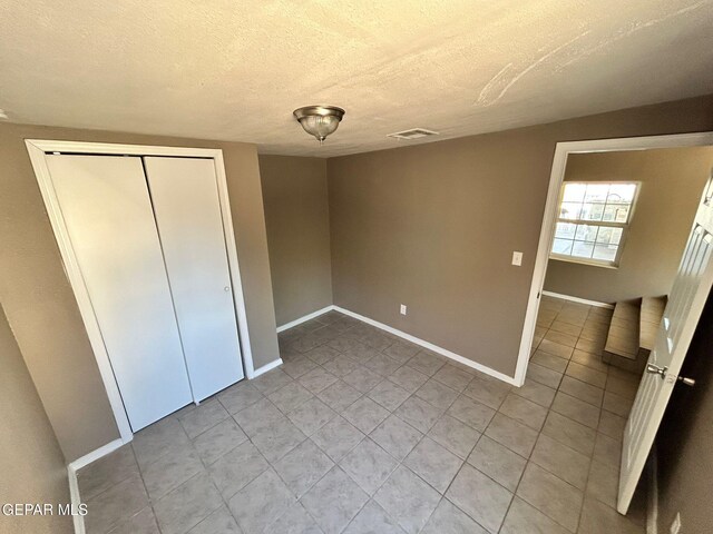 3416 Rivera Ave, El Paso, TX 79905 - unfurnished bedroom with light tile patterned floors, baseboards, a textured ceiling, and a closet