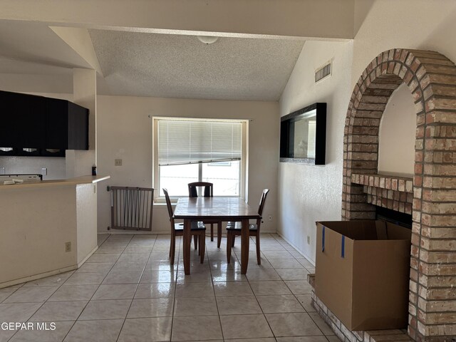 10645 Obsidian St, El Paso, TX 79924 - dining area with light tile patterned floors, a textured ceiling, vaulted ceiling, baseboards, and a brick fireplace