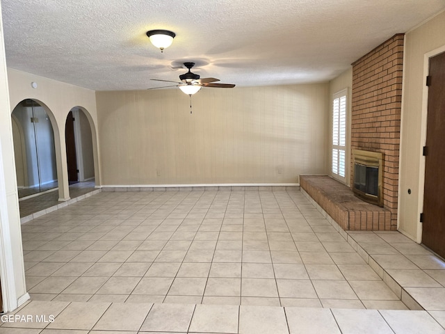 unfurnished living room with a ceiling fan, a fireplace, a textured ceiling, baseboards, and arched walkways