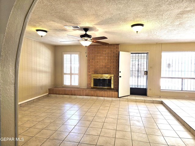 unfurnished living room featuring a ceiling fan, healthy amount of natural light, light tile patterned floors, a fireplace, and a textured ceiling
