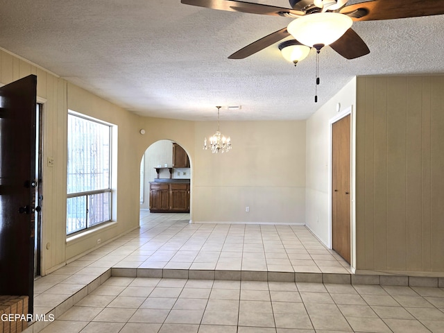 empty room featuring light tile patterned floors, arched walkways, a chandelier, wood walls, and a textured ceiling