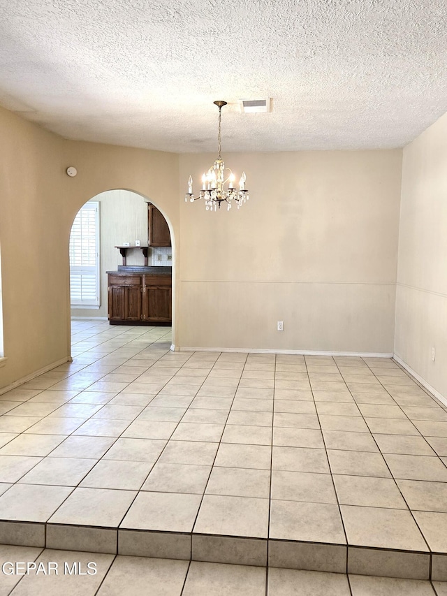 empty room featuring arched walkways, a chandelier, light tile patterned floors, and a textured ceiling