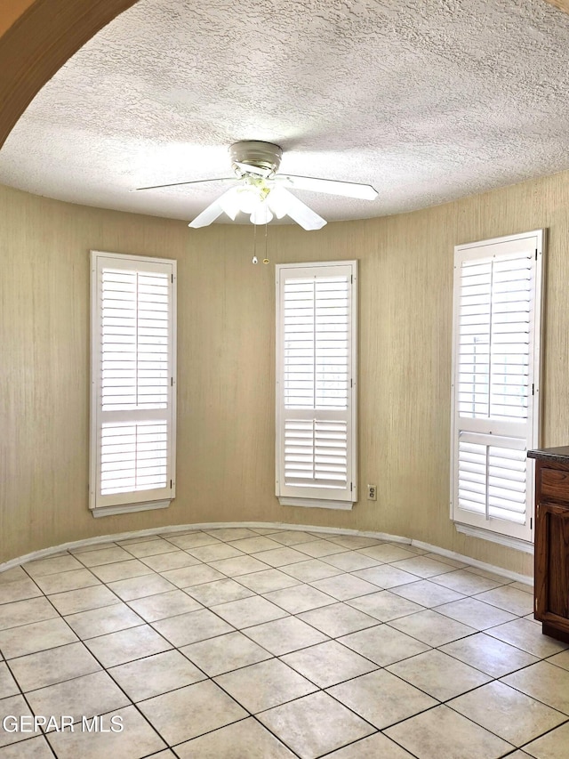 empty room featuring a textured ceiling, a ceiling fan, and light tile patterned floors