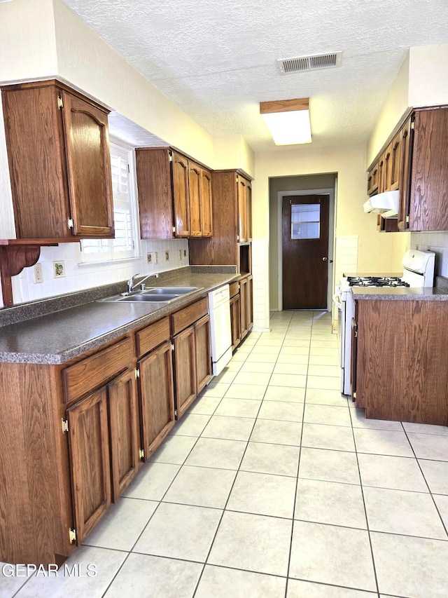 kitchen featuring white appliances, a sink, under cabinet range hood, dark countertops, and light tile patterned flooring