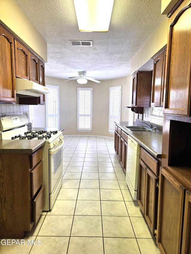 kitchen featuring white appliances, under cabinet range hood, a sink, a textured ceiling, and light tile patterned flooring