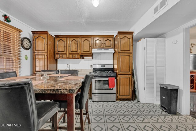 8715 Lawson St, El Paso, TX 79904 - kitchen featuring stainless steel range with gas cooktop, under cabinet range hood, brown cabinetry, light flooring, and light countertops