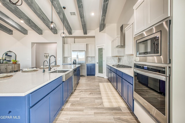 309 Blue Vly, El Paso, TX 79928 - kitchen with appliances with stainless steel finishes, blue cabinetry, wall chimney range hood, a sink, and beam ceiling