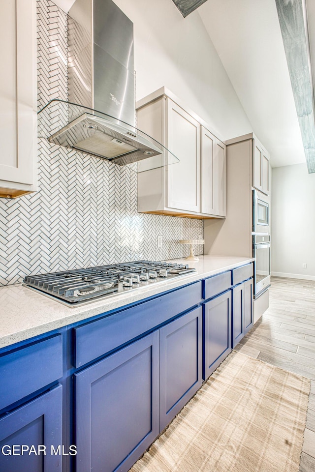 309 Blue Vly, El Paso, TX 79928 - kitchen featuring wall chimney range hood, stainless steel appliances, blue cabinetry, and backsplash