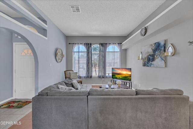 tiled living area with arched walkways, a textured ceiling, and baseboards