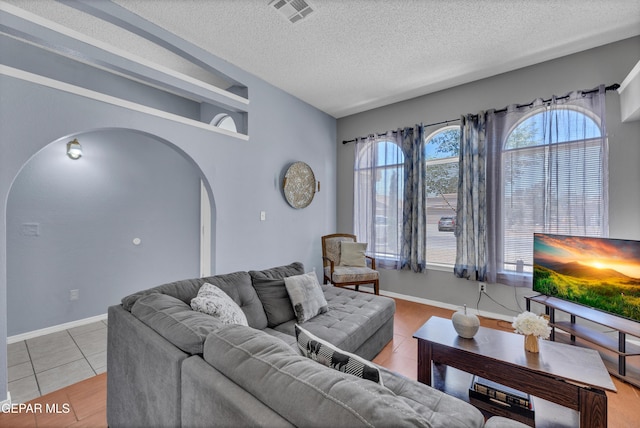 living area with arched walkways, a textured ceiling, light tile patterned floors, and baseboards