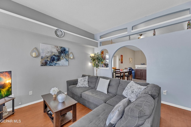 living room featuring arched walkways, wood finished floors, a textured ceiling, and baseboards