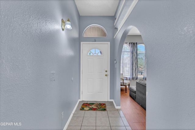 foyer entrance with light tile patterned floors, a textured wall, arched walkways, and baseboards