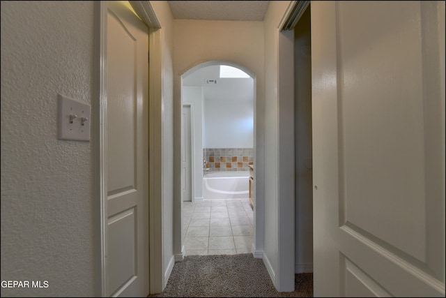 1493 Luz De Sol Dr, El Paso, TX 79912 - hallway featuring arched walkways, light tile patterned flooring, light carpet, a textured wall, and baseboards