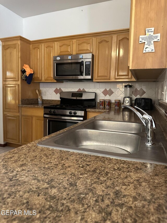14045 Lago Seco Dr, Horizon City, TX 79928 - kitchen featuring appliances with stainless steel finishes, dark countertops, a sink, decorative backsplash, and brown cabinets