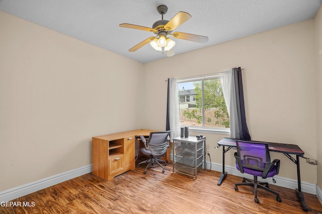 office area featuring light wood-style floors, baseboards, ceiling fan, and a textured ceiling