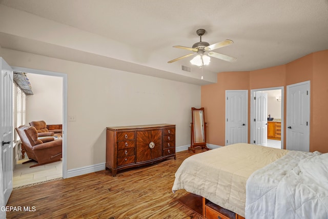 bedroom with wood finished floors, baseboards, a ceiling fan, and ensuite bathroom