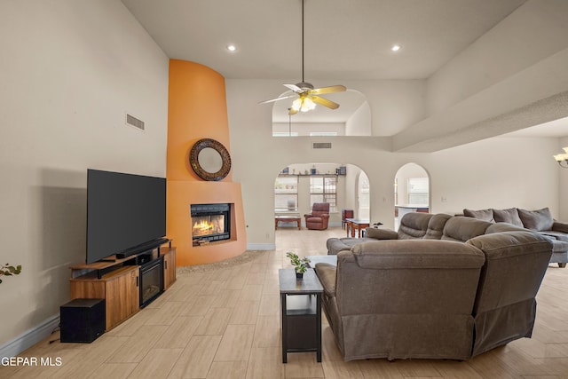 living area with a large fireplace, a high ceiling, a ceiling fan, baseboards, and recessed lighting